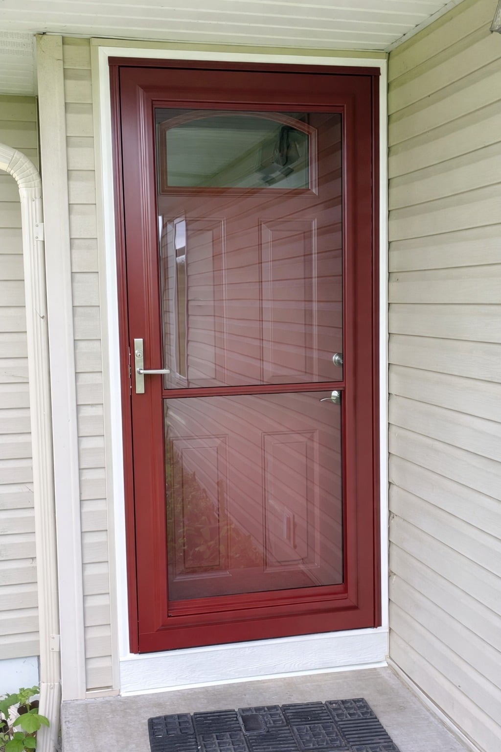 Red aluminum storm door installed on a residential home with light-colored siding and decorative upper glass panel