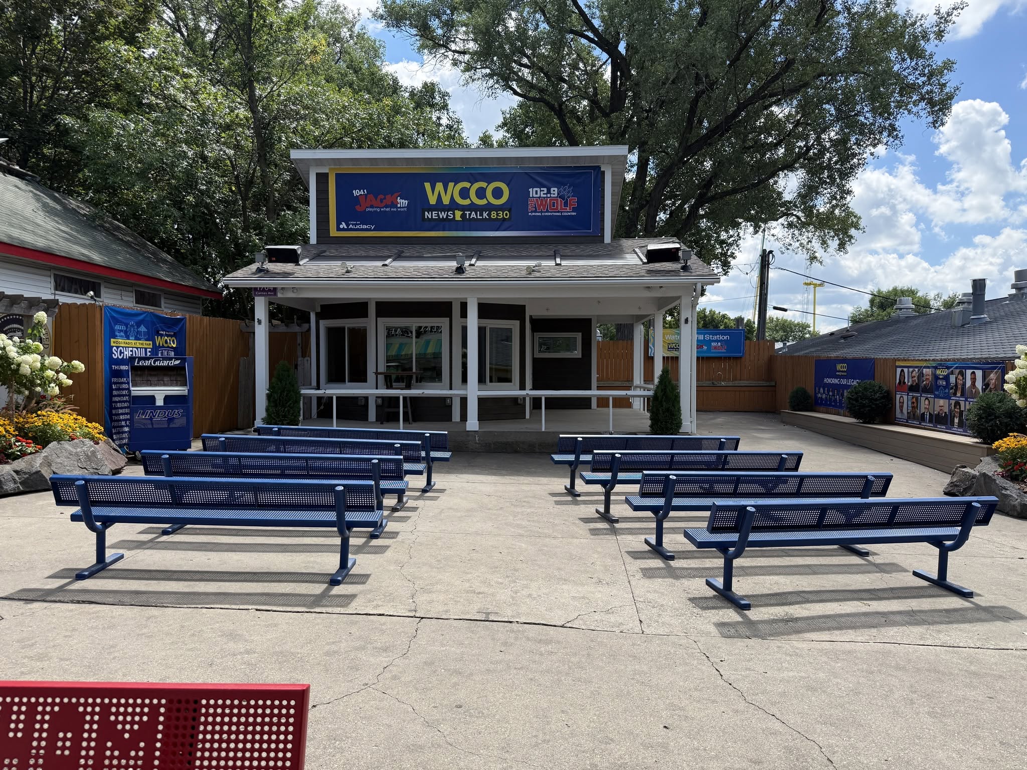 WCCO Radio booth at the Minnesota State Fair before the StruXure pergola installation, showing an uncovered outdoor seating area with rows of benches.